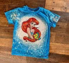 the little mermaid shirt is blue and has an image of ariel from the little mermaid on it