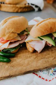 two sub sandwiches sitting on top of a wooden cutting board