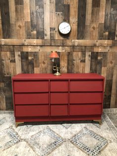 a red dresser sitting in front of a wooden wall with a clock on the side