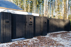 a row of black wooden restrooms next to a white house in the woods with snow on the ground