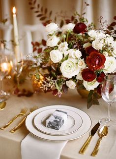 the table is set with white and red flowers, gold place settings, and candles