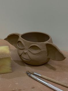 a clay mask and some paintbrushes on a table next to a pottery bowl