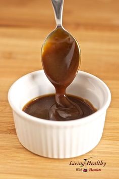 a spoon full of caramel sauce in a small white bowl on a wooden table