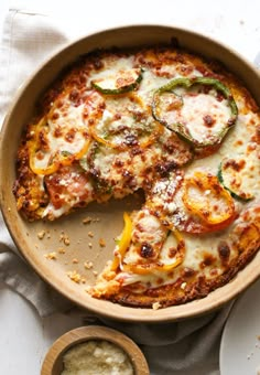 a pizza in a pan on top of a white table cloth next to a wooden spoon