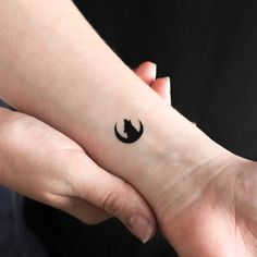 two hands holding each other with a small tattoo on the wrist that has a black star and moon