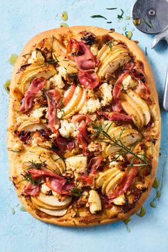 an uncooked pizza topped with meat and vegetables on a blue surface next to utensils