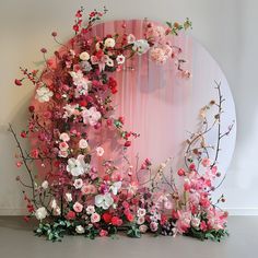 pink and white flowers are arranged in front of a circular wall with sheer drapes