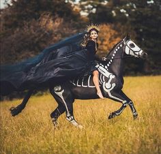 a woman riding on the back of a black horse in a field with tall grass