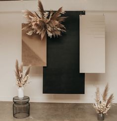 two vases with dried plants in front of a black and white wall