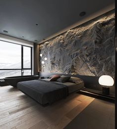 a bedroom with a large stone wall next to a bed and floor lamp in front of it