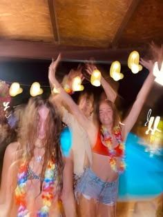 three young women dancing at a party with their arms in the air and lights above them