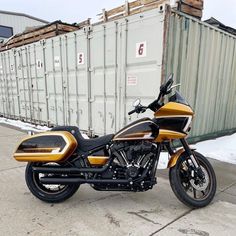 a gold and black motorcycle parked in front of a shipping container on the side of the road