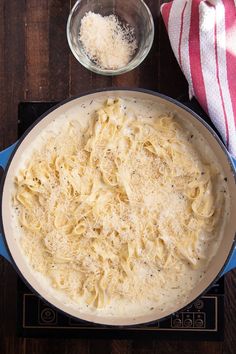 a pan filled with pasta on top of a stove next to a bowl of grated parmesan cheese