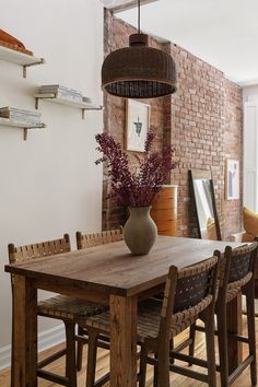 a dining room table with chairs and a vase on top of it in front of a brick wall