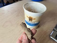 a hand holding a piece of food next to a cup of coffee on a table