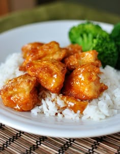 a white plate topped with chicken and rice next to broccoli on a table