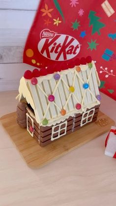 a cake shaped like a house on a wooden board next to a red flag with the kfc's logo