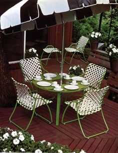 an outdoor table and chairs with umbrellas on the decking in front of flowers