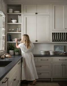 a woman is standing in the kitchen looking at dishes