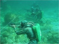 two people in scuba gear are on the rocks and one person is holding a camera