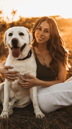 a woman sitting on the ground with her dog in front of her and smiling at the camera