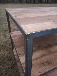 a wooden table sitting on top of a field next to a grass covered field with trees in the background