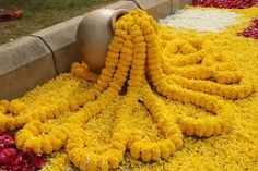 yellow and red flowers on the ground next to a metal vase with water in it