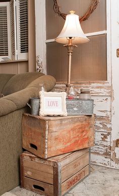 two wooden boxes stacked on top of each other in front of a couch with a lamp