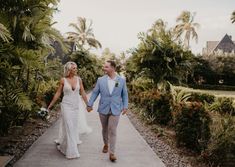 a bride and groom walking down a path in the middle of palm trees holding hands