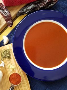 a bowl of tomato soup on a wooden cutting board next to garlic and seasoning