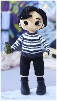 a knitted doll with black and white striped shirt holding a green object in his hand