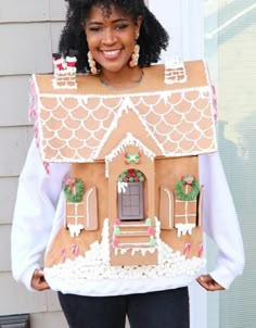 a woman holding up a gingerbread house made to look like it's been built