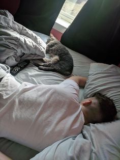 a man laying in bed next to a cat on top of his head and sleeping