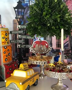 a table topped with cakes and desserts next to a yellow taxi car cake stand