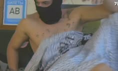 a shirtless man wearing a black mask and covering his face with a gray blanket