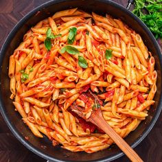 a pan filled with pasta and sauce on top of a wooden table next to parsley