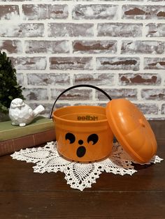 an orange pail with a face painted on it sitting next to some books and a potted plant