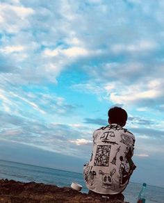 a man sitting on top of a beach next to the ocean under a cloudy blue sky