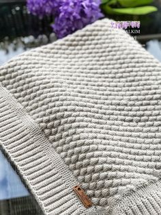 a white knitted blanket sitting on top of a table next to purple flowers in a vase