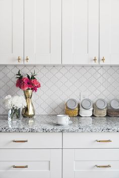 a kitchen with white cabinets and marble counter tops, gold vases on the island