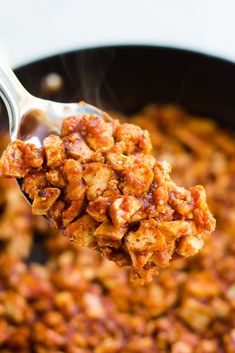 a spoon full of food is being lifted from a skillet with meat in it