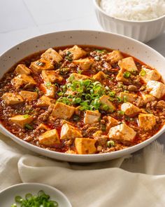 a white bowl filled with tofu and rice on top of a table next to two bowls