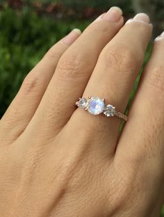 a woman's hand holding an engagement ring with three stones on the band and one stone in the middle