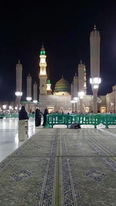 two people sitting on the ground in front of a building at night with lights shining