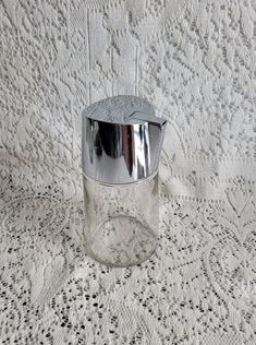 an empty glass jar sitting on top of a white tablecloth covered table with lacy doily