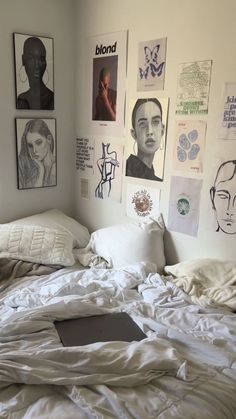 an unmade bed with white sheets and pictures on the wall above it, along with a laptop computer