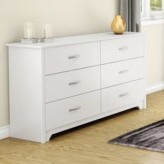 a white dresser sitting on top of a hard wood floor next to a large window