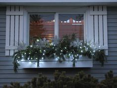 a window sill decorated with christmas lights and greenery in front of a house