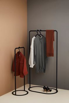 two clothes hangers with coats and shoes on them in front of a gray wall