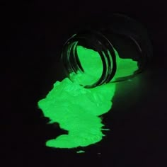 a green glow in the dark on a black surface with a small bottle next to it